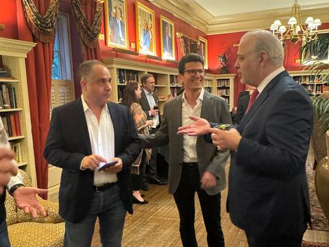 Three men chatting at a reception in the red library room