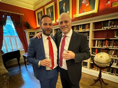 Two men in suits and red ties posing in a library with a globe