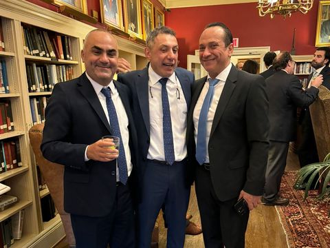 Three men in suits posing together in a library at a reception