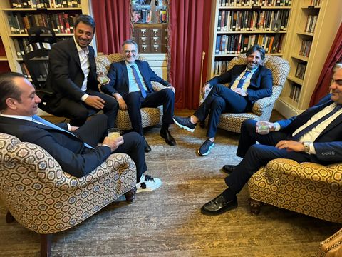 Five men seated in armchairs in a library, laughing and chatting