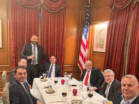 Seven men seated around a dinner table with a U.S. flag
